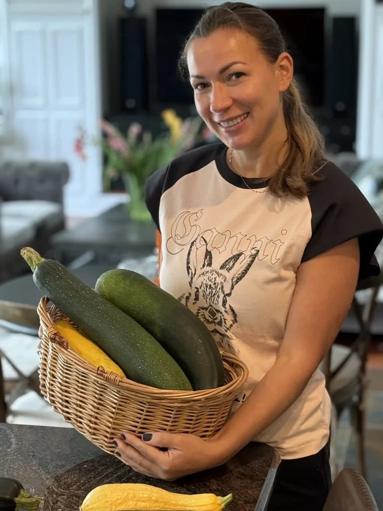 A woman smiling while holding a basket of fresh zucchini