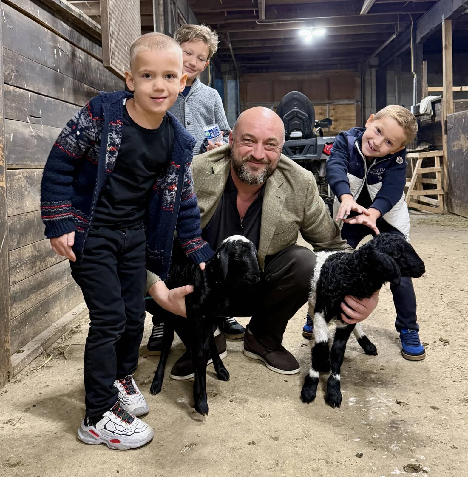 A dad and three kids in the barn with two baby goats