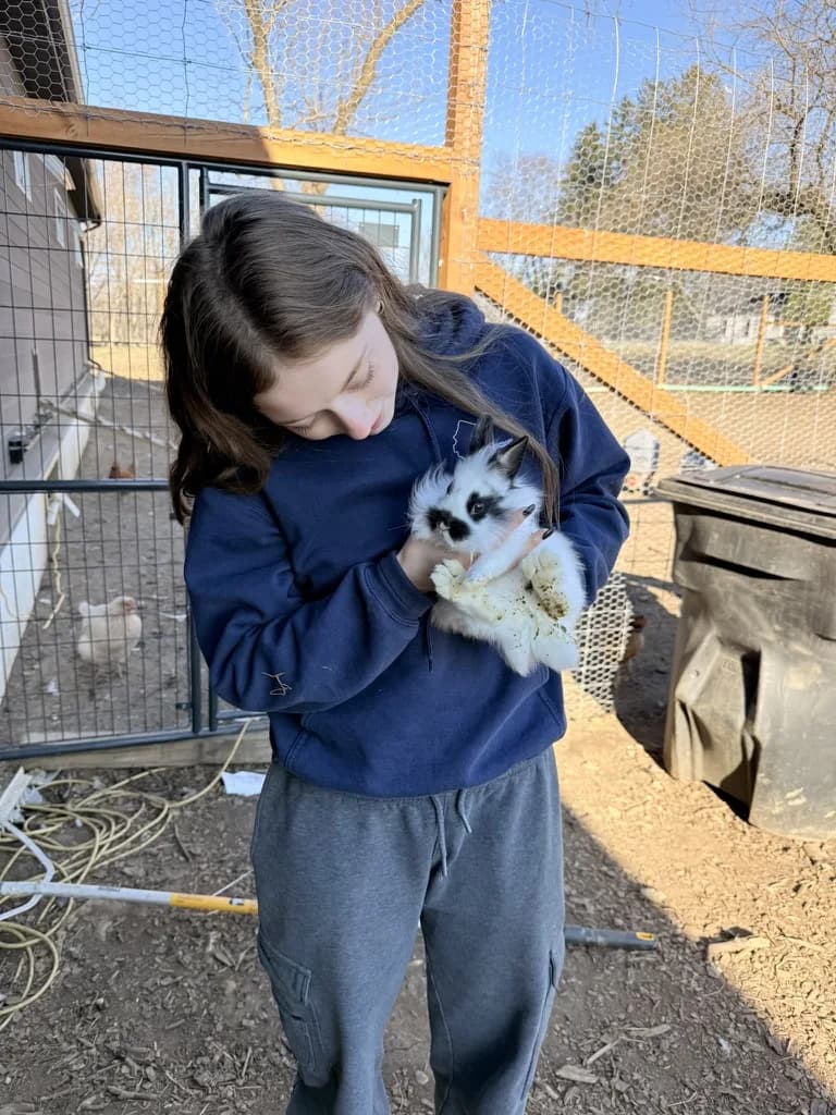 A girl standing in the coop, holding a pet rabbit