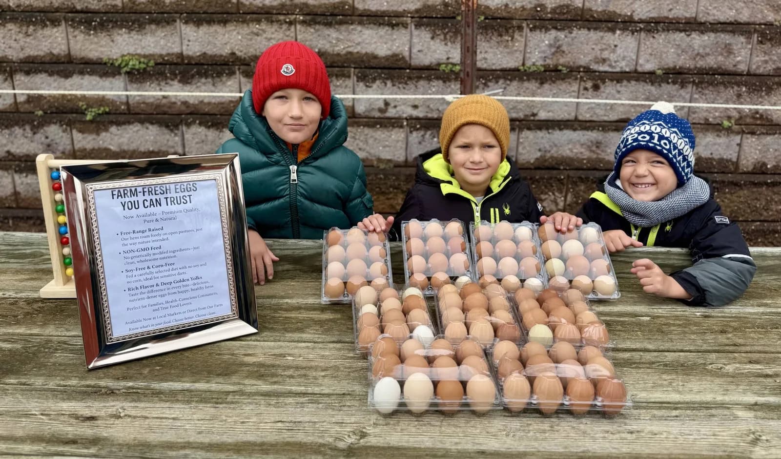 Three kids behind a hand-lettered farm-fresh egg stand